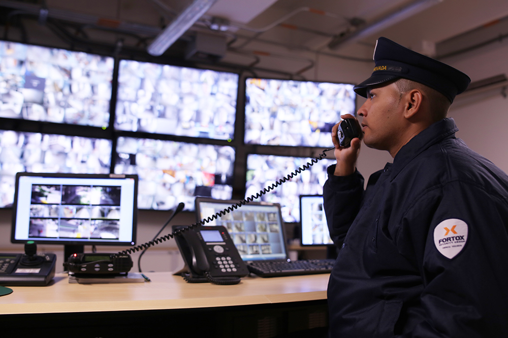 Guardia de seguridad privada Fortox monitororea cámaras de vigilancia en sala de control, usando radio para comunicación. - Fortox