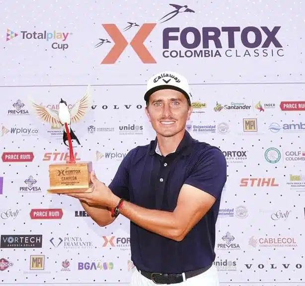 En la imagen aparece un golfista en uniforme sosteniendo un trofeo frente a una pared con los logotipos de los patrocinadores del evento Fortox Colombia Classic. - Fortox Security