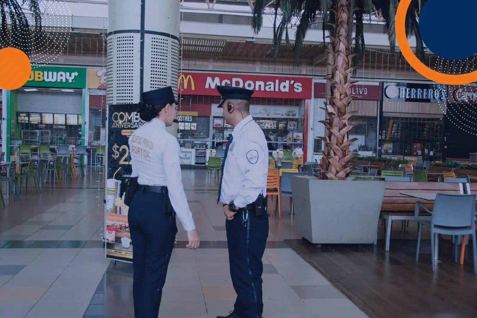 En la imagen se observan dos guardias de seguridad privada de Fortox conversando dentro de la plazoleta de comidas de un centro comercial. Al fondo, se pueden ver los letreros de los restaurantes Subway y McDonald’s. Los agentes de vigilancia están uniformados y atentos al entorno, brindando protección empresarial en el área. - Fortox Security