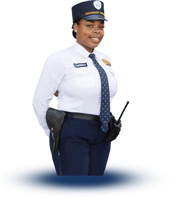 En la imagen se observa a una guardia de seguridad privada de Fortox. Ella viste uniforme completo, con gorra, corbata y distintivo en el brazo. Lleva una radio y una funda en el cinturón. Se encuentra de pie, mirando al frente y con las manos detrás de la espalda, transmitiendo profesionalismo y vigilancia en su trabajo de protección empresarial. No hay vehículos ni edificios visibles; el enfoque principal es el personal de seguridad. - Fortox Security