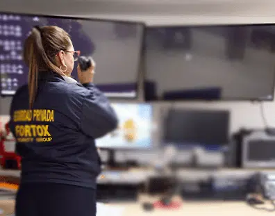 Guardia de seguridad privada de Fortox monitorea cámaras de vigilancia y se comunica por radio en el centro empresarial moderno. - Fortox Security