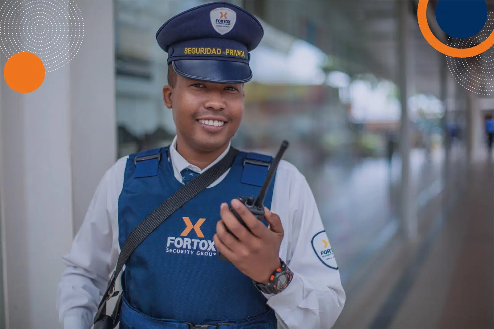Guardia de seguridad privada de Fortox con uniforme y radio, en interiores junto a pared de vidrio durante labores de vigilancia empresarial. - Fortox Security