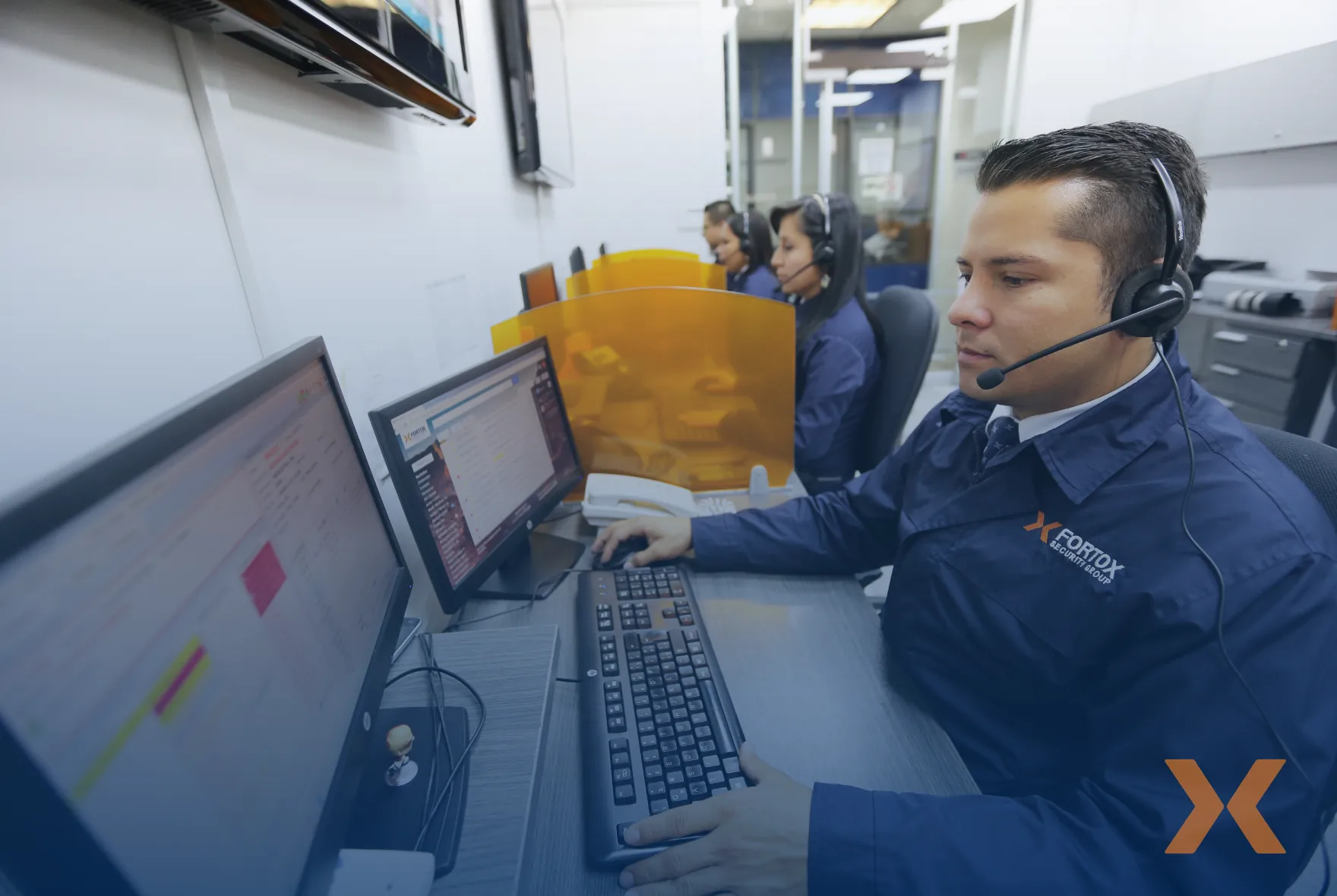 Hombre con auriculares opera un computer en centro de control de seguridad privada Fortox, junto a otros agentes en vigilancia. - Fortox