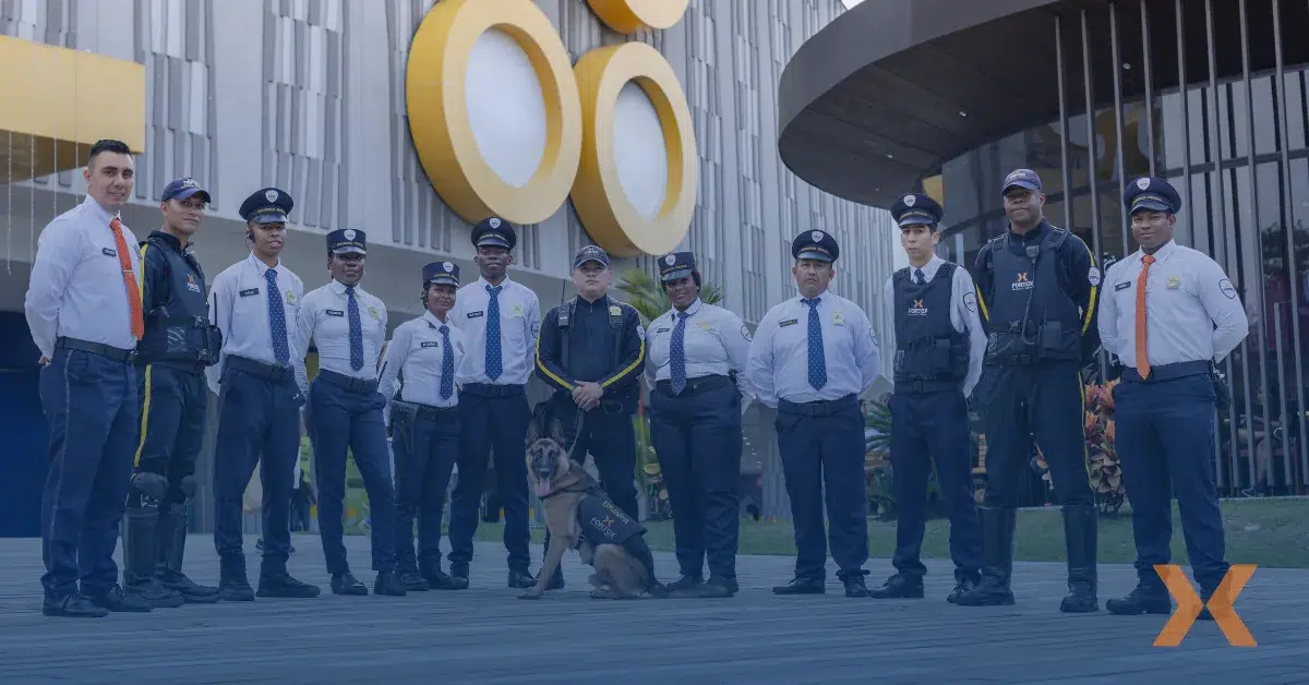 Un grupo de vigilantes y un oficial con perro frente a edificio moderno, mostrando seguridad privada y vigilancia profesional Fortox. - Fortox
